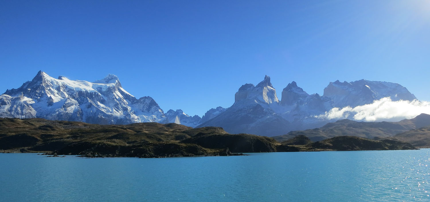 A Chilean Patagonia yacht charter sails on blue water with a snowy mountain backdrop